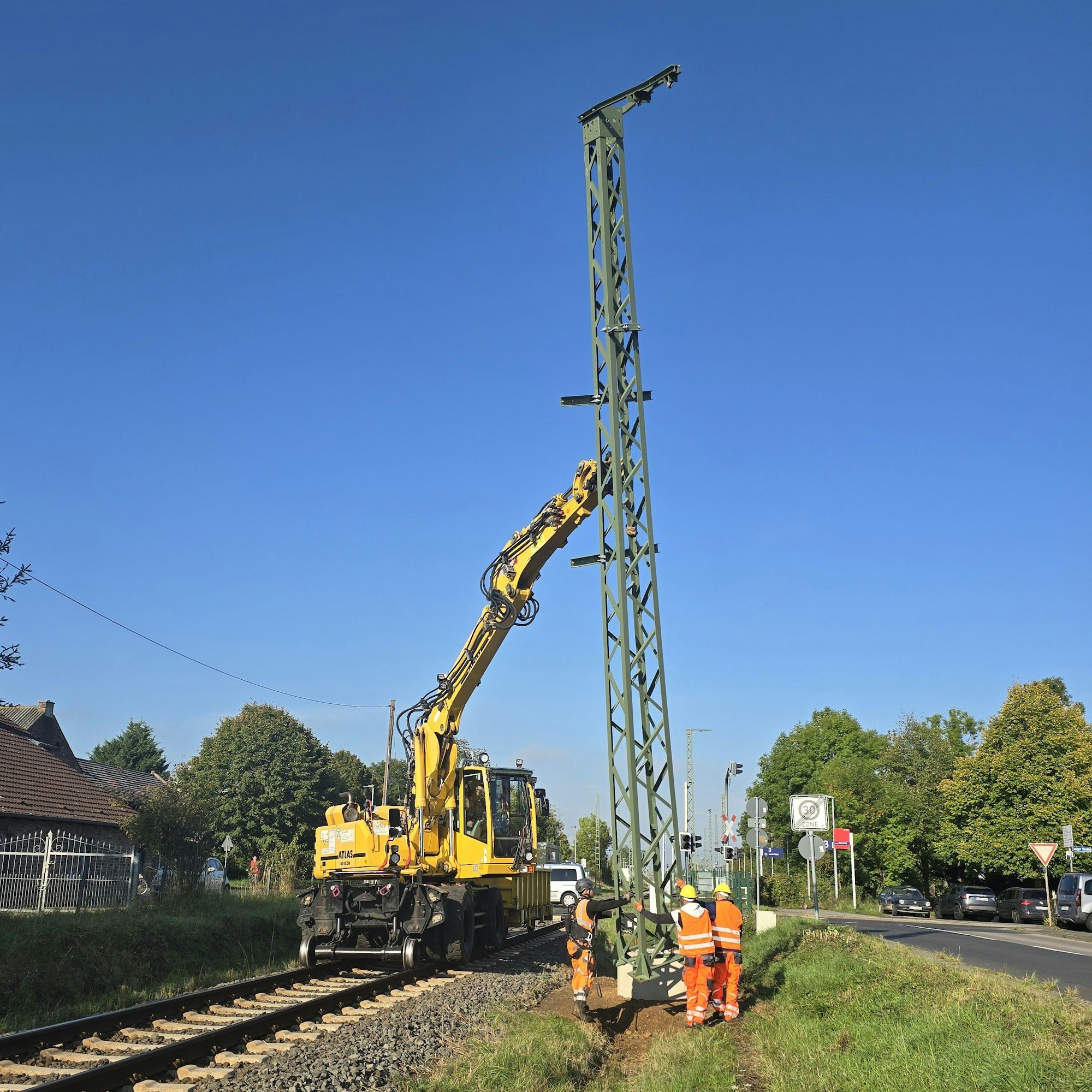 Bahnarbeiter montieren den Mast der Oberleitung, der von einem Kran aufgerichtet worden ist.
