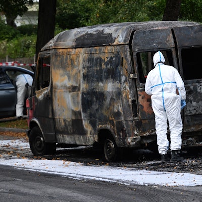 Ein Beamter der Spurensicherung untersucht einen ausgebrannten Transporter in München.