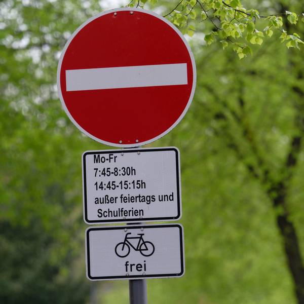 In Köln weist ein Schild auf eine Sperrung einer Straße während der Bring- und Abholzeit einer in der Straße gelegenen Grundschule für den Autoverkehr hin.
