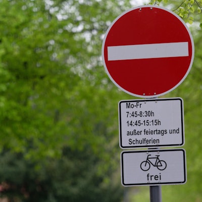 In Köln weist ein Schild auf eine Sperrung einer Straße während der Bring- und Abholzeit einer in der Straße gelegenen Grundschule für den Autoverkehr hin.
