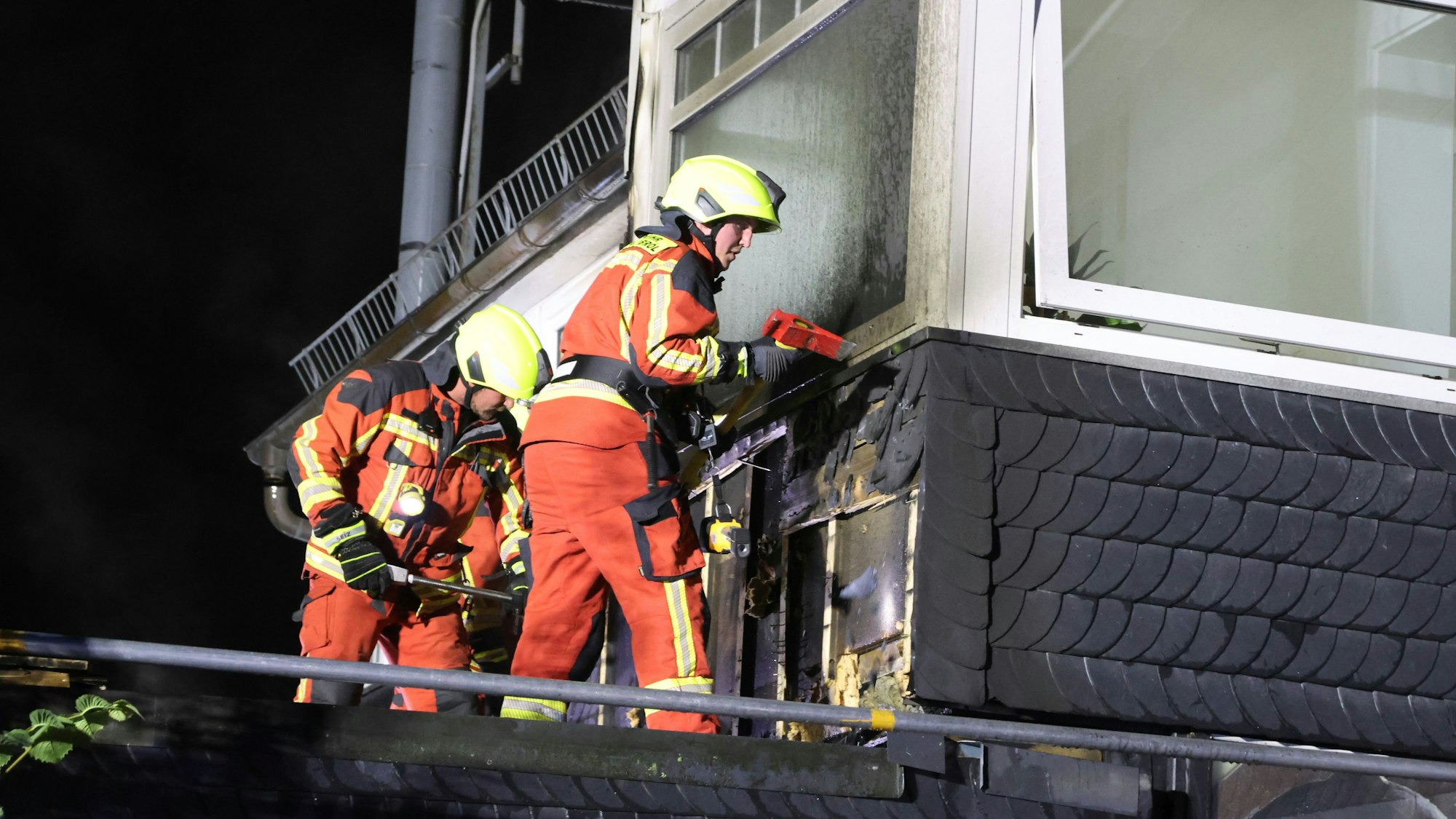 Ein Feuerwehrmann schlägt mit einer Axt eine Schieferverkleidung auf.