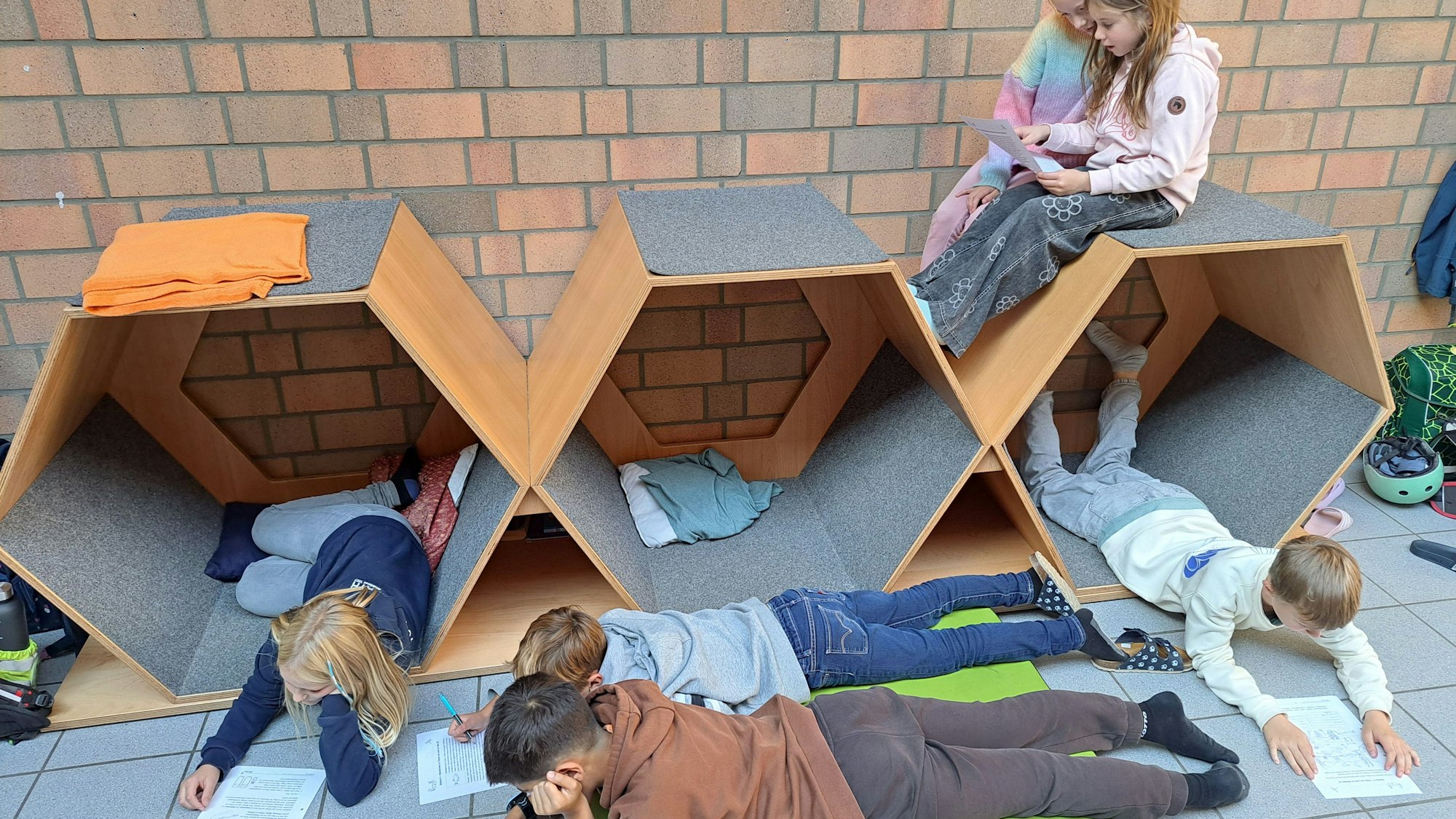 Kinder lernen liegend auf Matten und sitzend auf Sechseck-Elementen