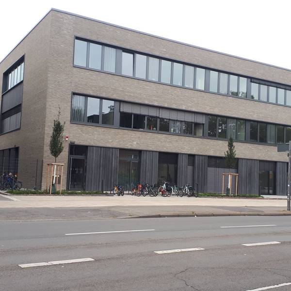Ein dreistöckiges flaches Gebäude steht an einer mehrspurigen Straße.