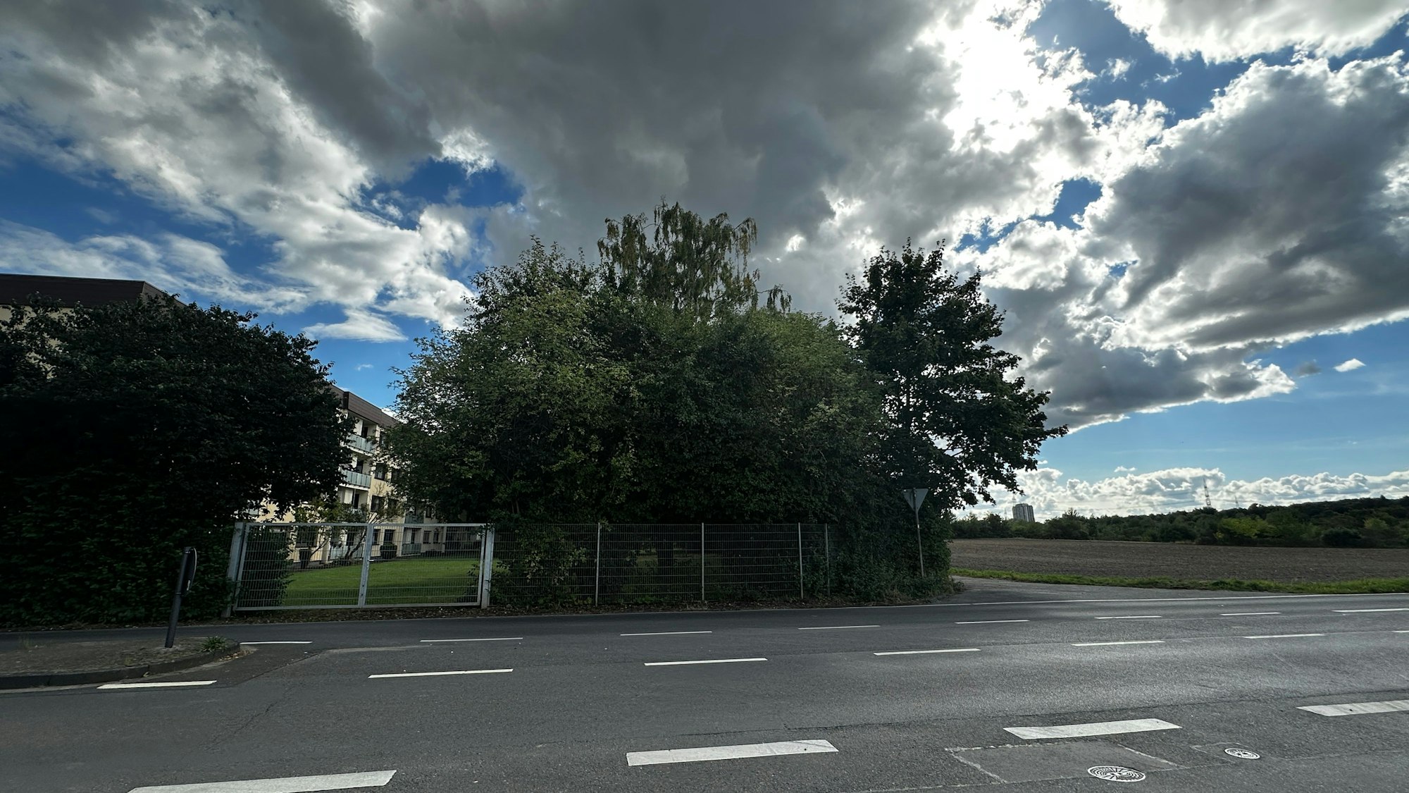 Eine zweispurige Straße und eine Einmündung, an der mehrgeschossige Wohnhäuser liegen, ist zu sehen.