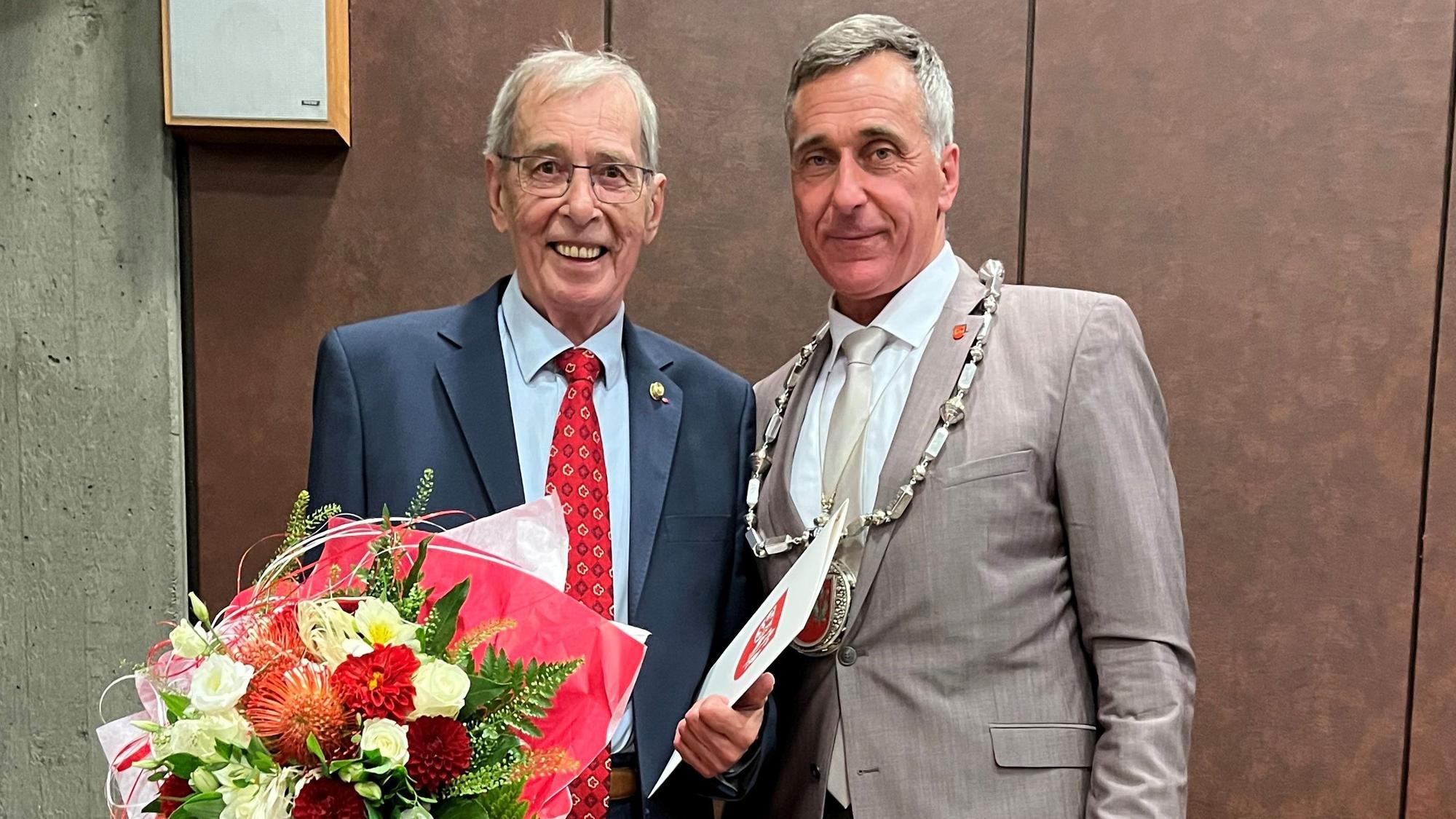 Zwei Männer stehen nebeneinander, einer hält einen großen Blumenstrauß.