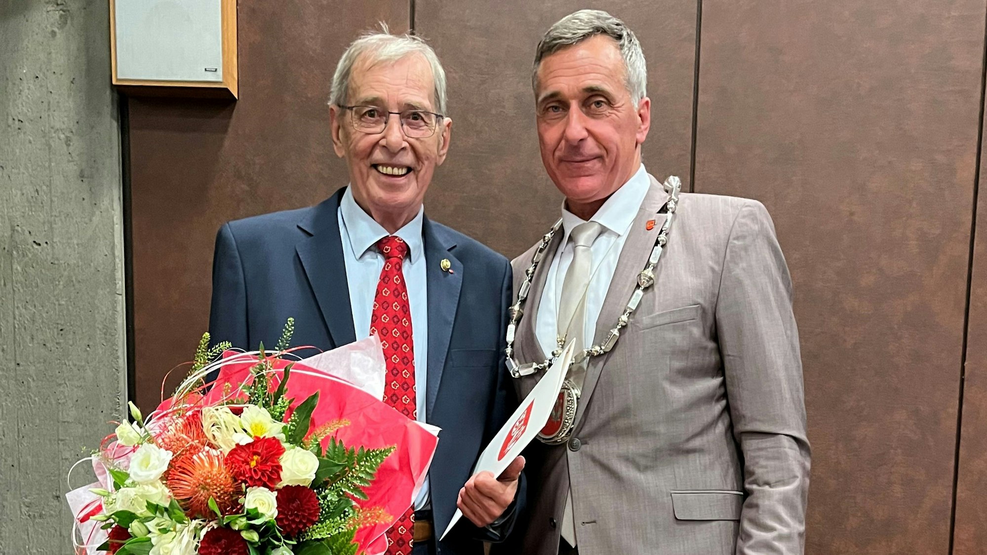 Zwei Männer stehen nebeneinander, einer hält einen großen Blumenstrauß.