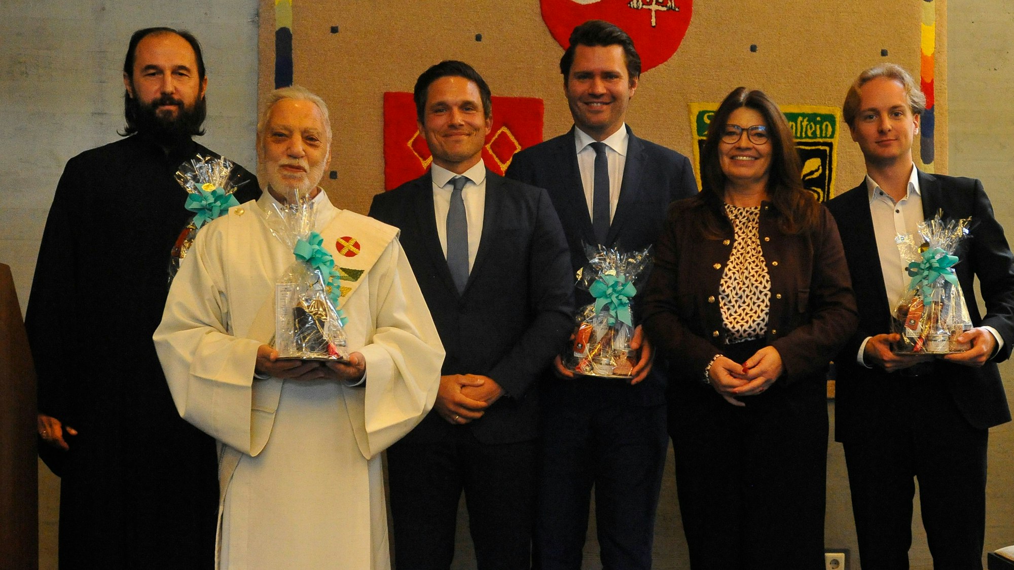 Männer und eine Frau stehen nebeneinander, vier halten Präsente.