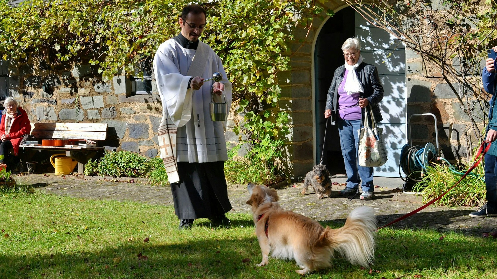 Diakon Francesco Tabacco, der ein liturgisches Gewand trägt, besprengt einen kleinen Hund mit Weihwasser.