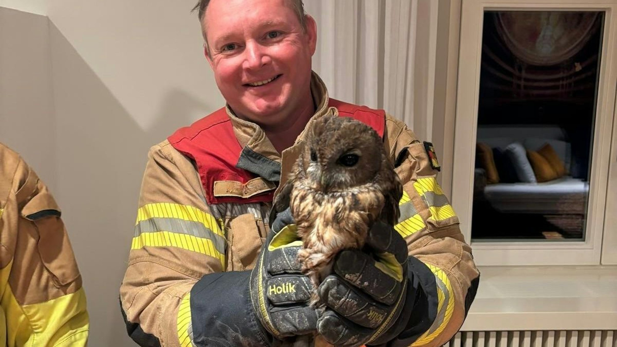 Ein Feuerwehrmann hält einen verrußten Waldkauz in den Händen.