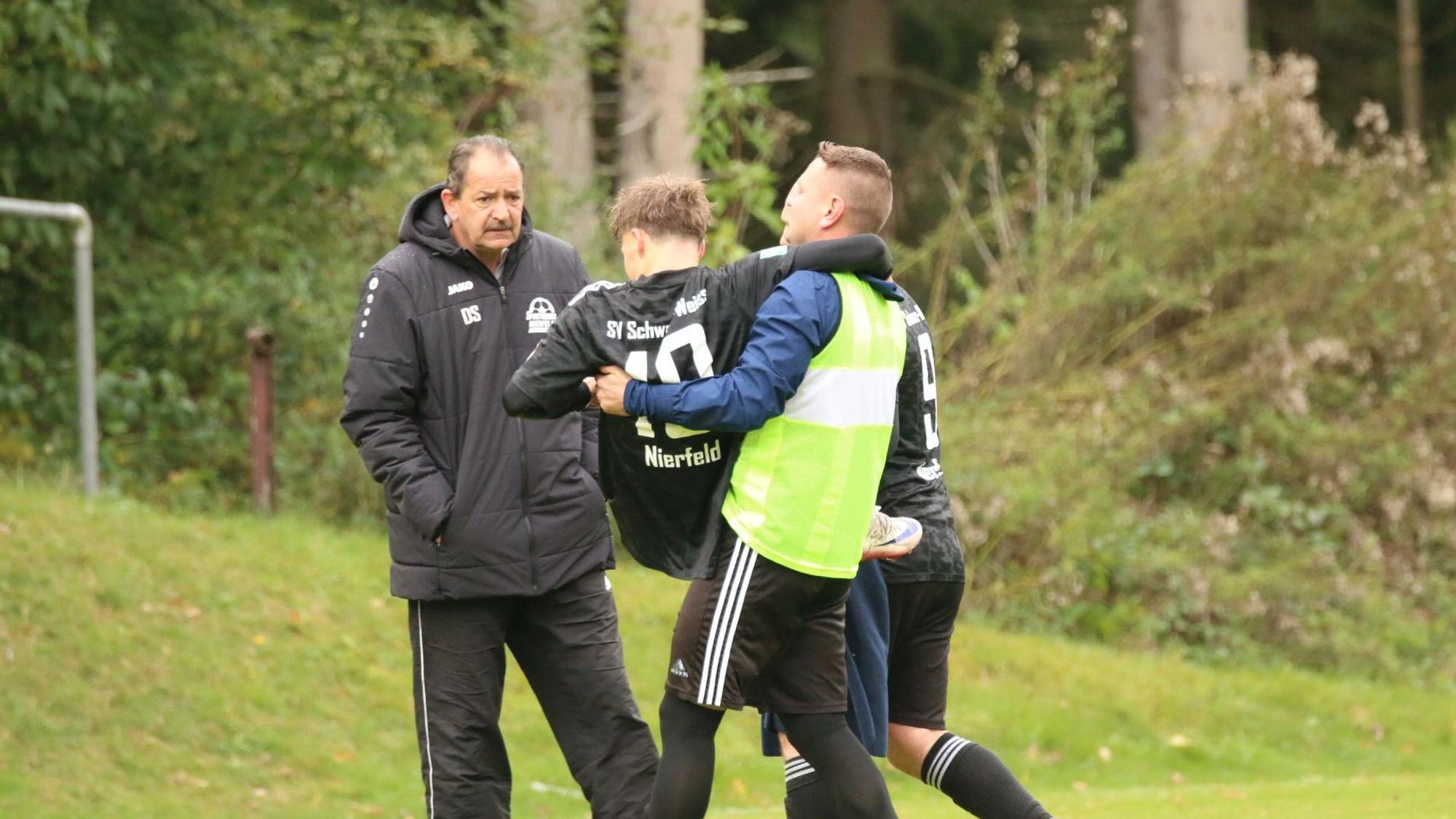 Zwei Mitspieler bringen den verletzten Akteur zum Spielfeldrand.