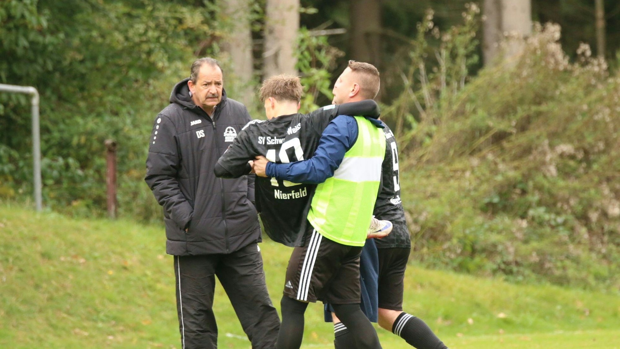 Zwei Mitspieler bringen den verletzten Akteur zum Spielfeldrand.