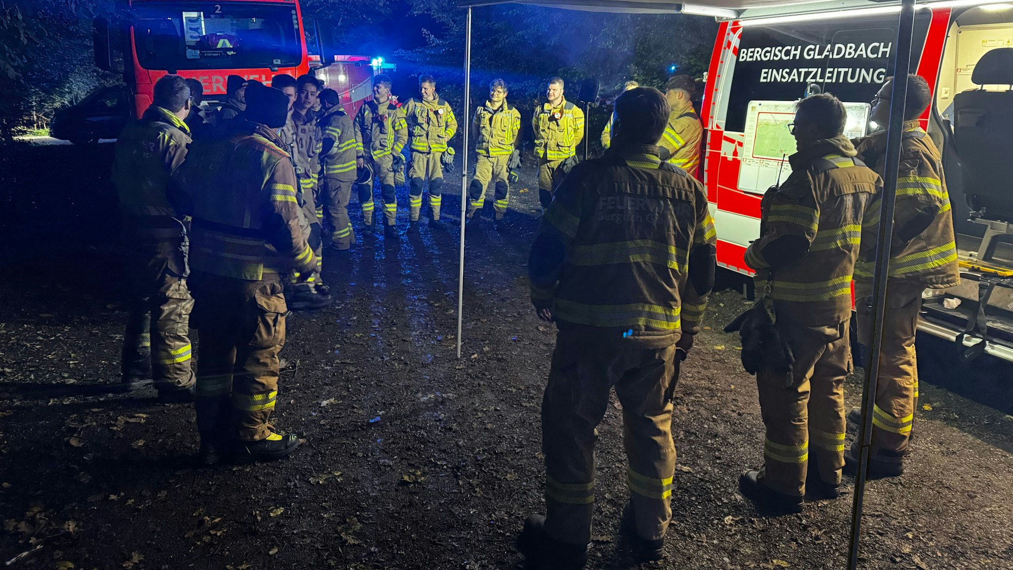 Feuerwehrleute stehen an Einsatzfahrzeugen nachts im Wald.