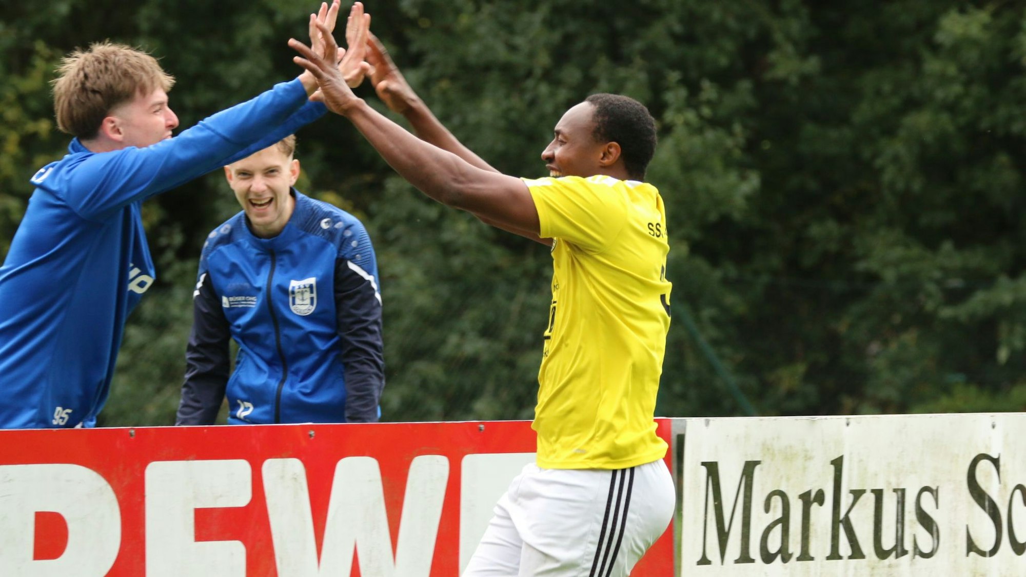 Zwei Spieler klatschen sich ab, ein anderer schaut zu. Alle lachen fröhlich.