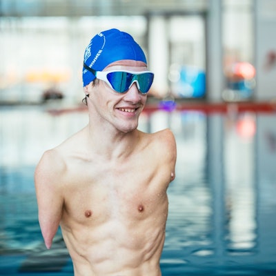 Janis McDavid trägt eine blaue Haube und eine Schwimmbrille. Neben ihm ein Mann mit blauem T-Shirt. Im Hintergrund ein Schwimmbad.