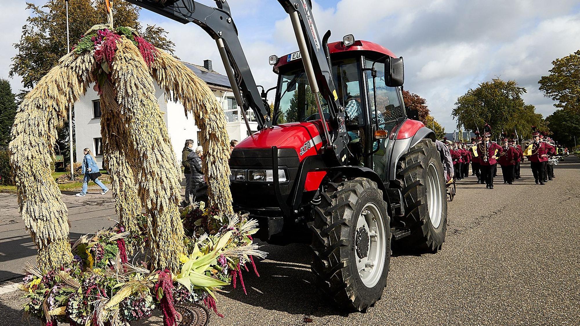 Ein Traktor hat eine Strohfigur am Frontlader hängen. Hinter dem Gefährt marschiert ein Spielmannszug.