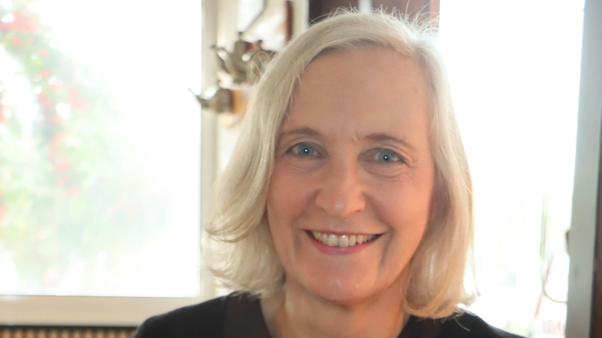 Eine blonde Frau sitzt vor einem Fenster.