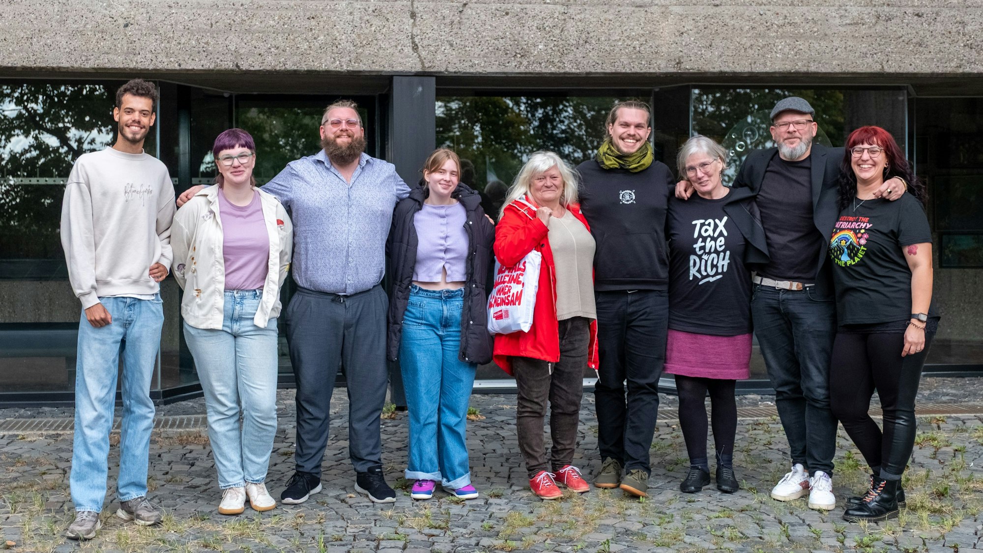Menschen stehen vor dem Bensberger Rathaus und haken sich teilweise unter.