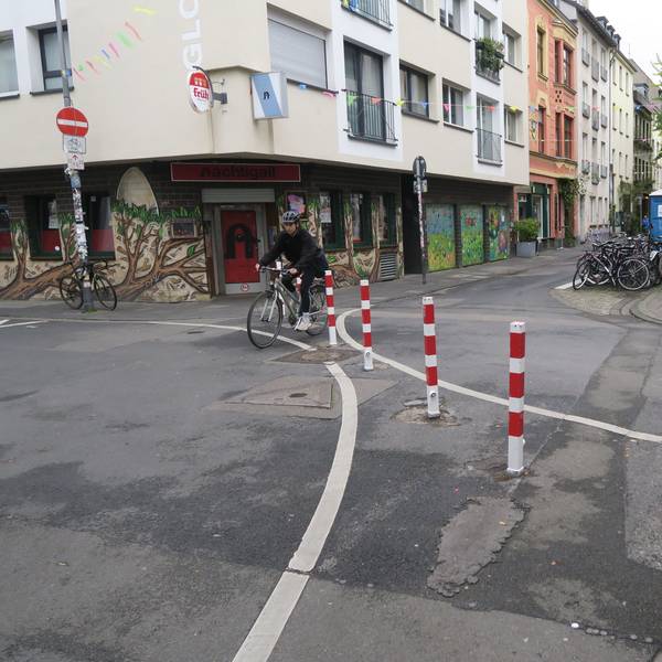 Auf einer Kreuzung zweier schmaler Straßen stehen rot-weiße-Poller.