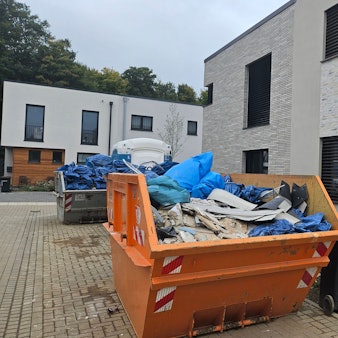 Zu sehen sind mit Sperrmüll gefüllte Container in einer Neubausiedlung.