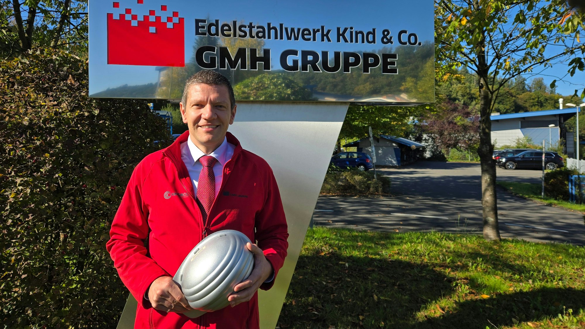 Ein Mann im roten Kittel vor dem Firmenschild.