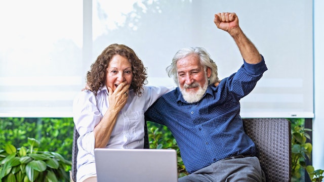 Eine Frau und ein Mann sitzen vor einem Laptop und freuen sich.