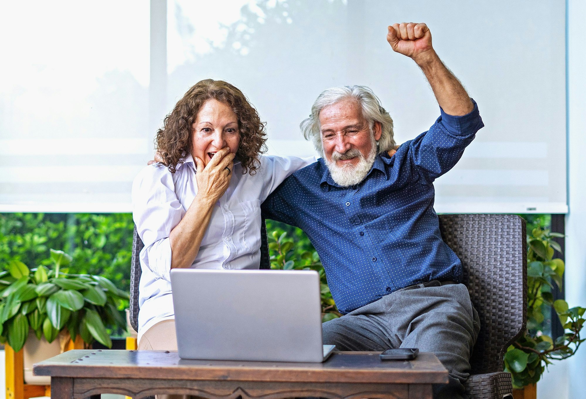 Eine Frau und ein Mann sitzen vor einem Laptop und freuen sich.