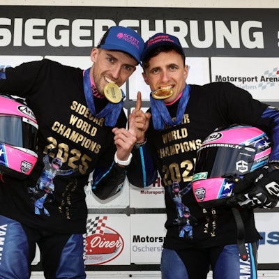 Zu sehen sind zwei Motorsportler, die auf Goldmedaillen beißen.