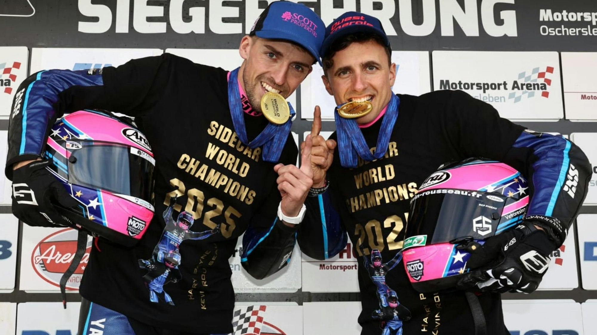 Zu sehen sind zwei Motorsportler, die auf Goldmedaillen beißen.