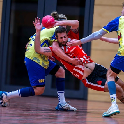 Von hinten umklammert ein Gegenspieler aus Eschweiler den werfenden David Henzel, dessen Bauch zu sehen ist.