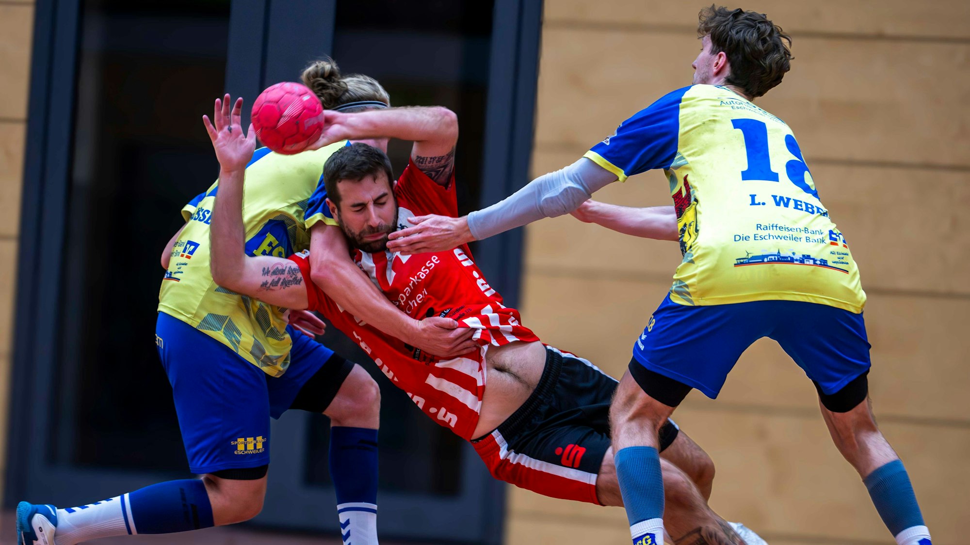 Von hinten umklammert ein Gegenspieler aus Eschweiler den werfenden David Henzel, dessen Bauch zu sehen ist.