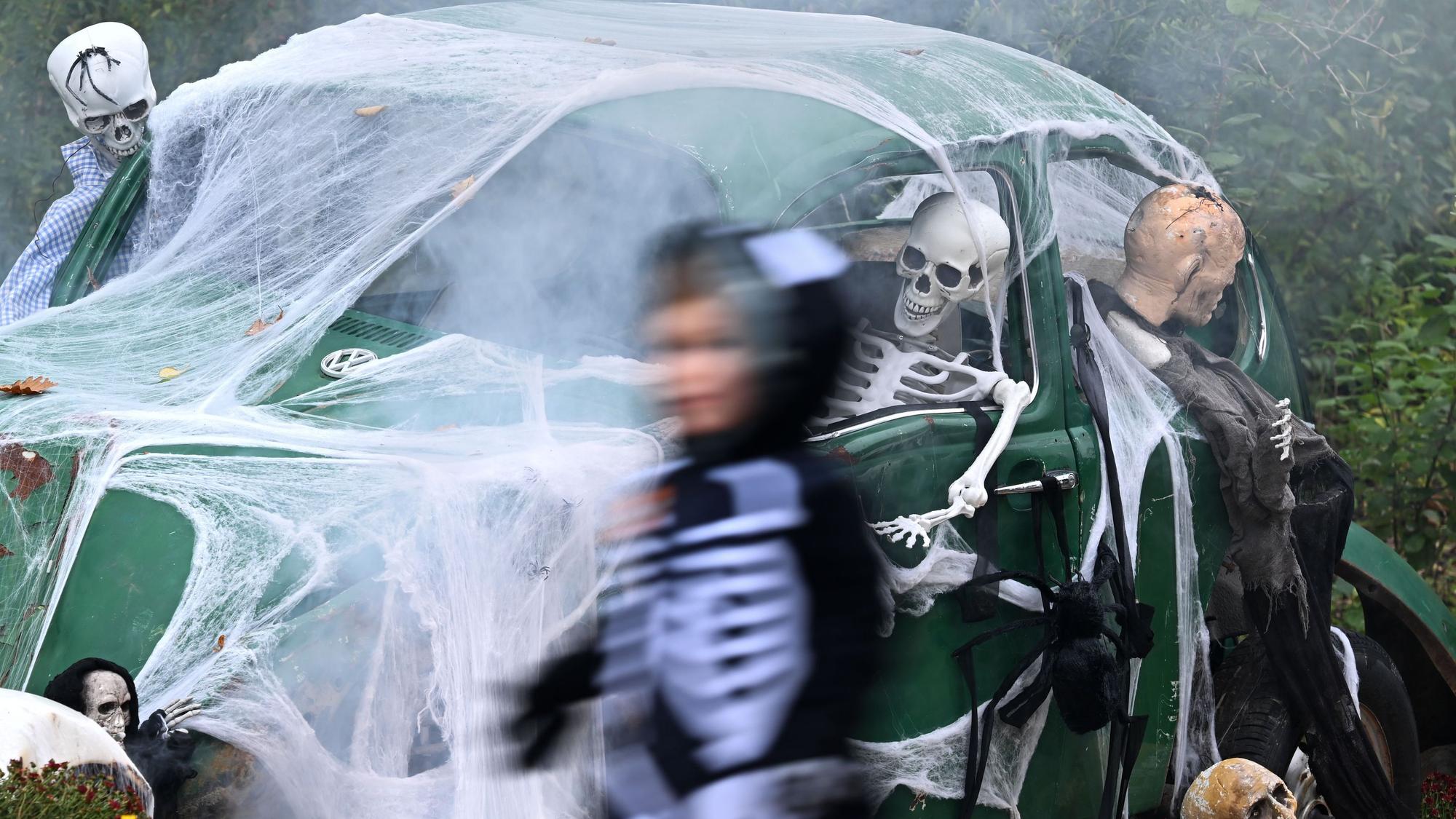 Ein Kind geht an einem zu Halloween mit Netz und Skeletten geschmückten alten VW Käfer vorbei. (Archivbild)