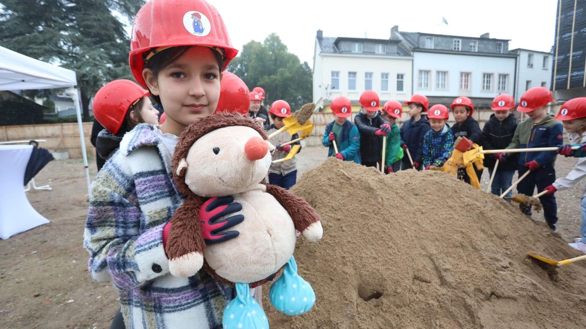 Ein Mädchen mit einer Maulwurfsfigur, im Hintergrund schaufeln ihre Mitschüler an einem Haufen Erde.