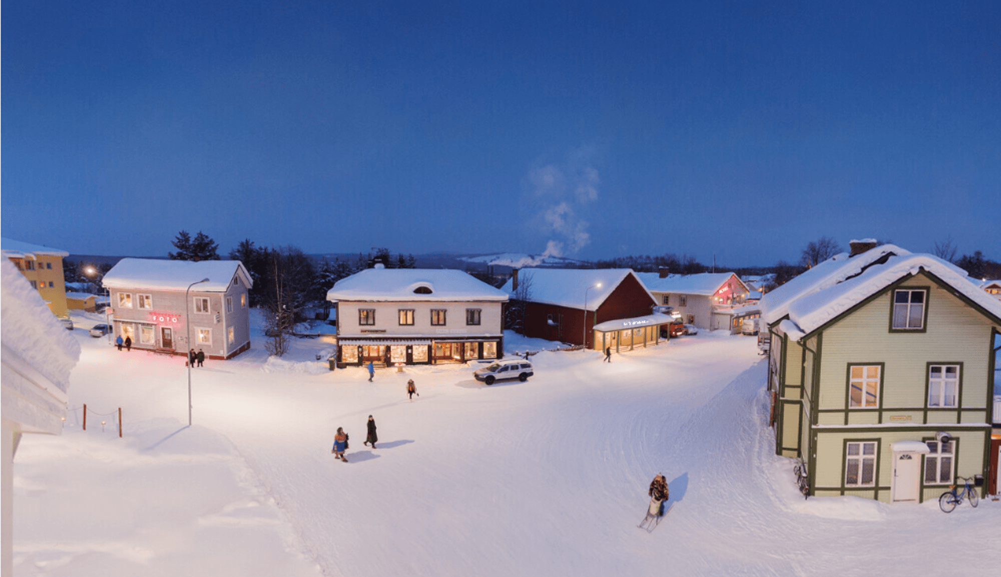 Das Bild zeigt ein verschneites Dorf in der Dämmerung. Warme Lichter erhellen die gemütlichen Holzhäuser, während Menschen durch den tiefen Schnee spazieren.