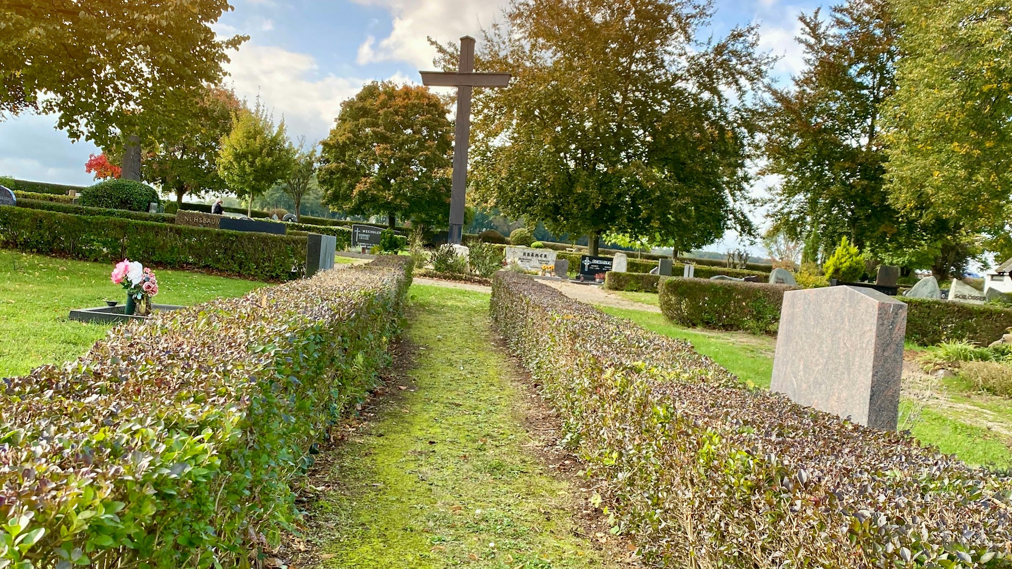 Ein Weg, den gestutzte Hecken säumen, führt zu einem Kreuz.