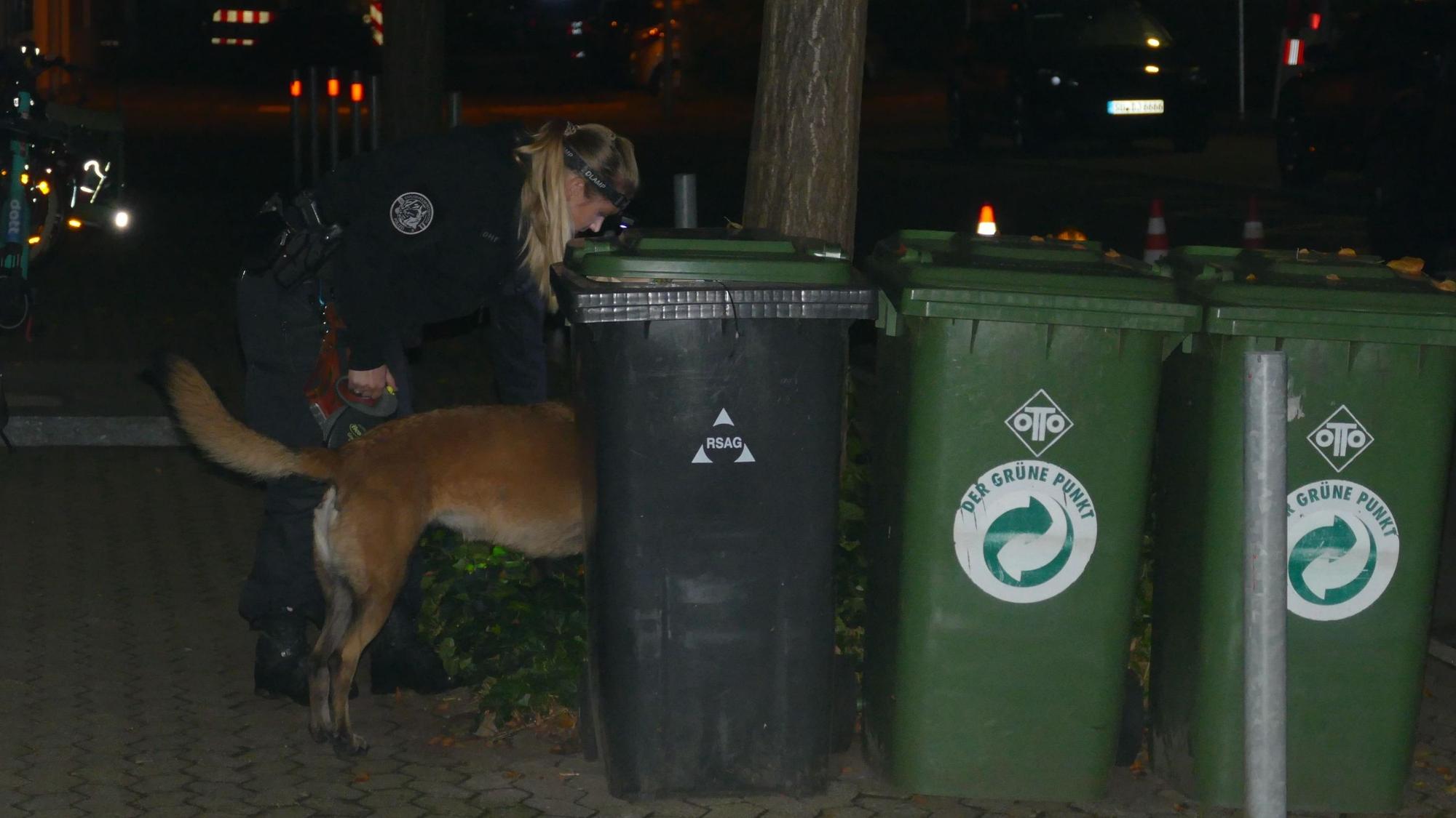 Eine Polizistin lässt einen Spürhund hinter Mülltonnen suchen.