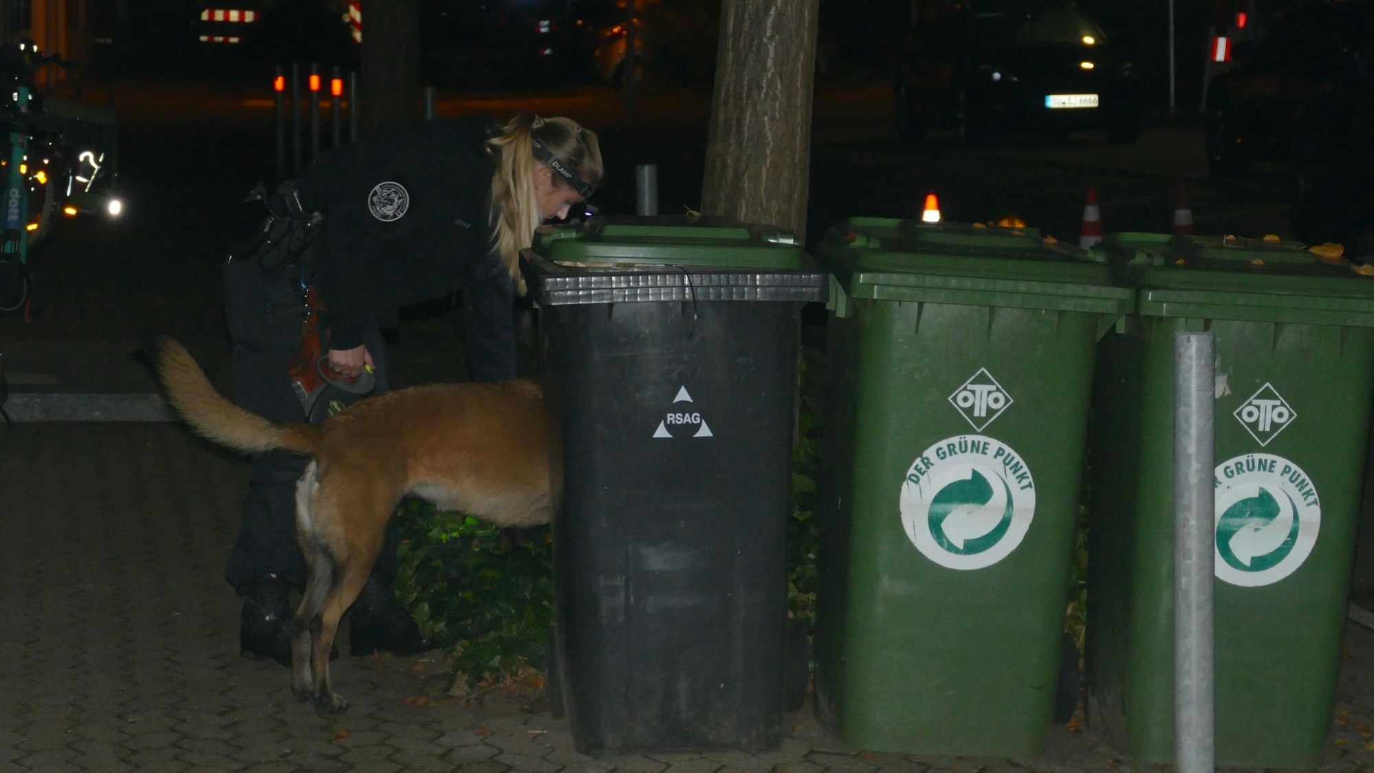 Eine Polizistin lässt einen Spürhund hinter Mülltonnen suchen.