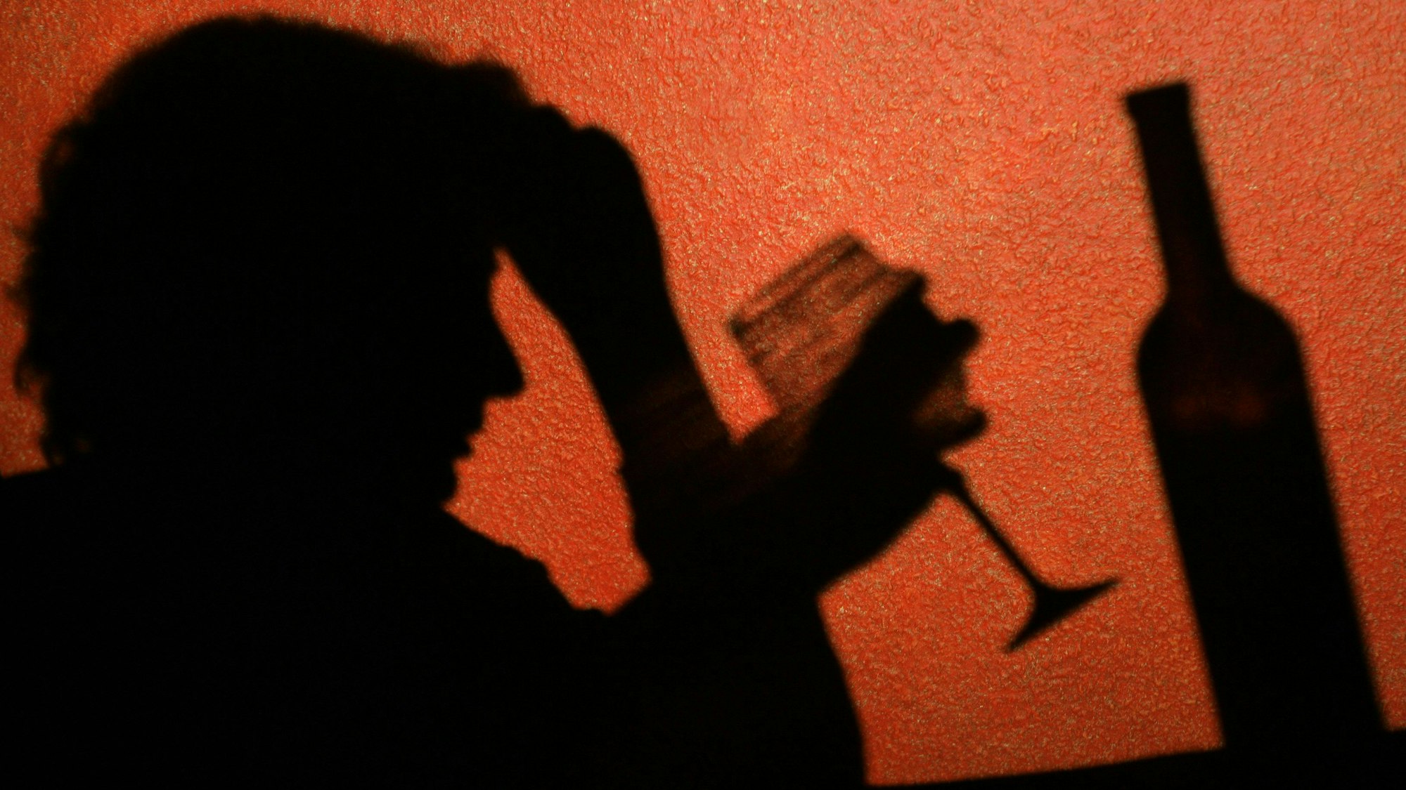 Der Schatten einer Frau, die ein Glas Wein trinkt, ist an der Wand zu erkennen, aufgenommen.