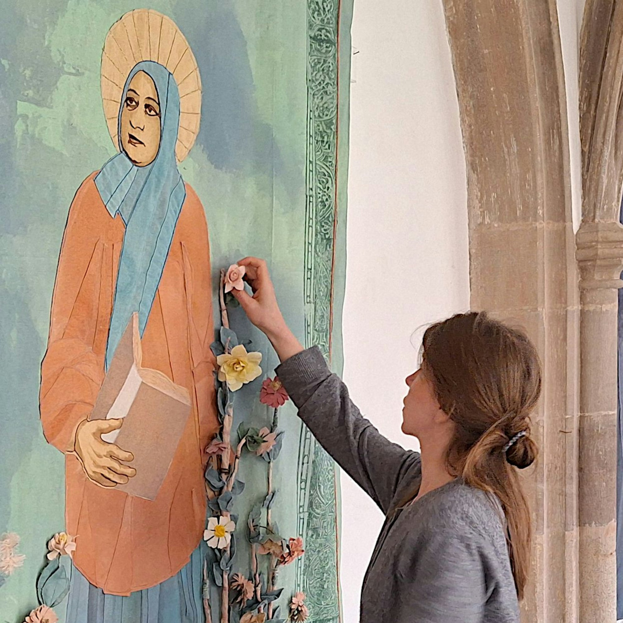 Monika von Bernuth justiert Blumen an einem Textilstück, auf dem Asmet Idrees als Heiliger dargestellt wird.