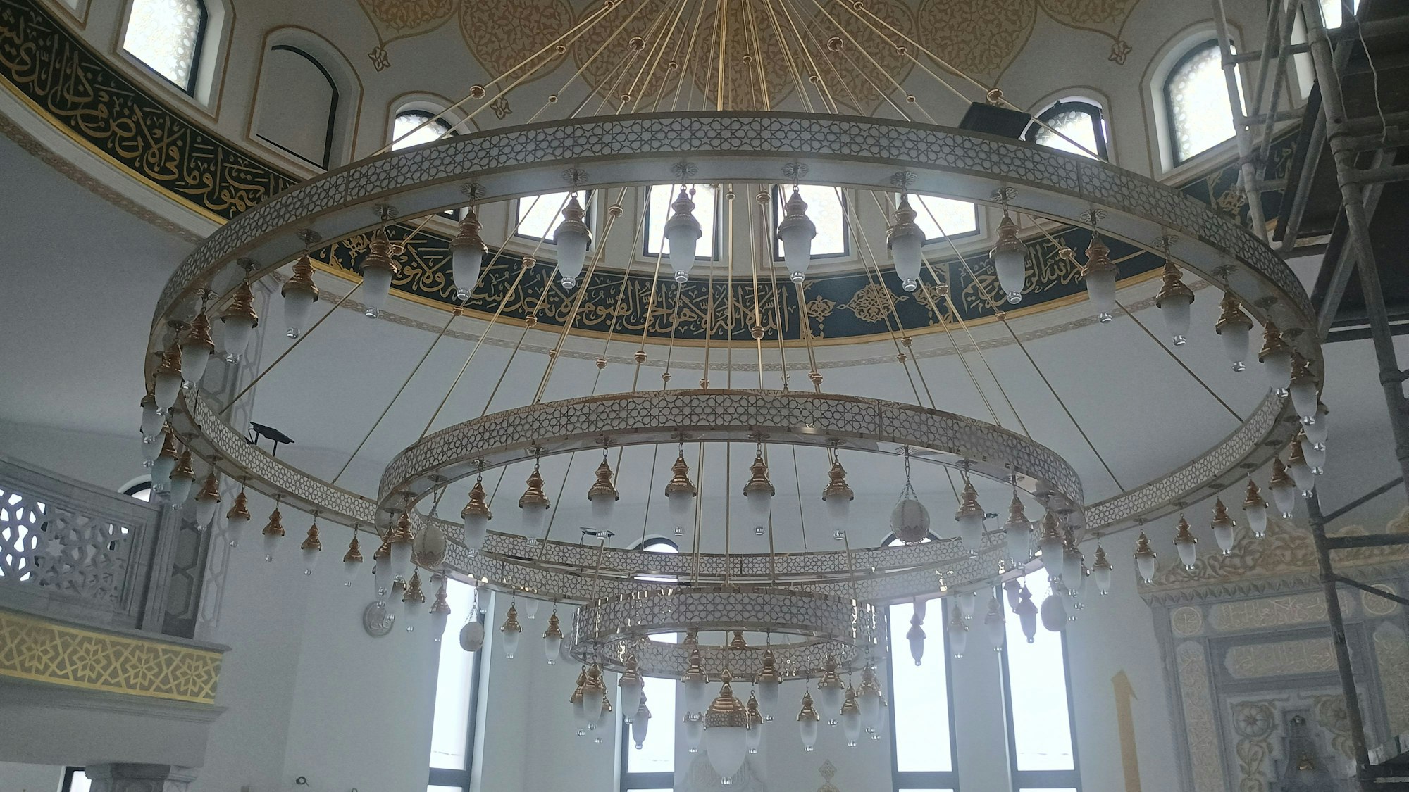 Der Kronleuchter ist mehrstufig und besteht aus mehreren Kreisen, an denen Lampen hängen.