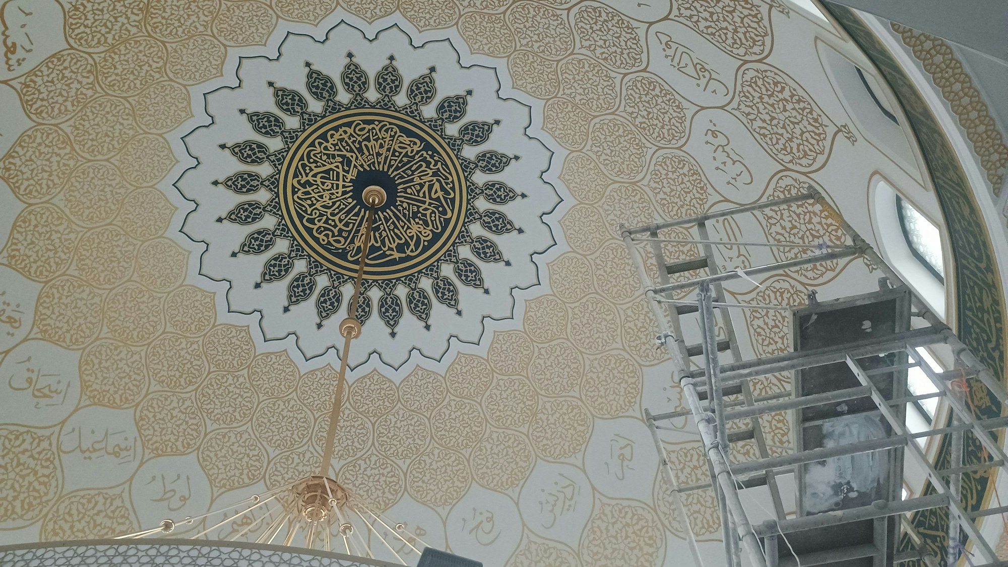 Wer nach oben in die Mitte des Kuppeldachs blickt, sieht ein kreisförmiges Medaillon, ebenfalls mit goldener Kalligrafie geschmückt, und drumherum ein florales Muster, das sternförmig über die gesamte Kuppel verläuft.