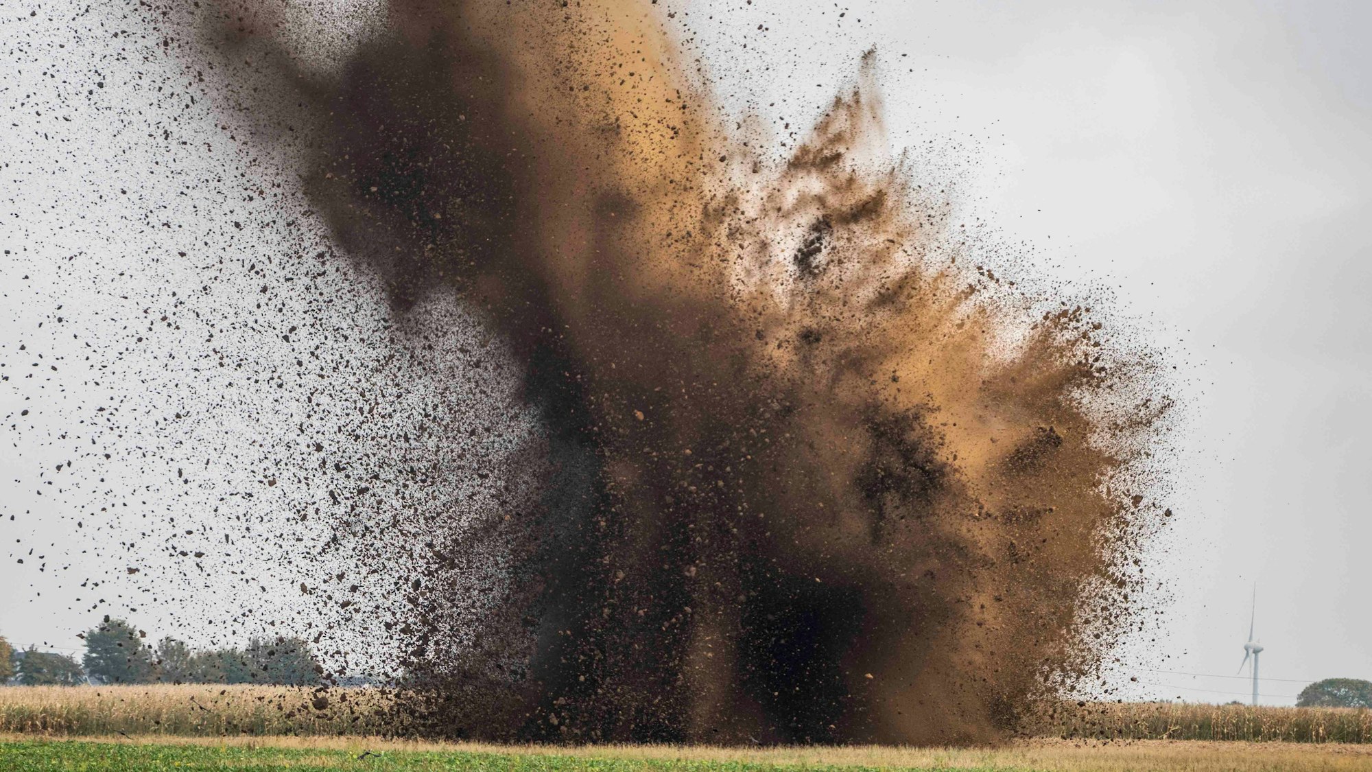 Auf einem Feld sieht man die Explosion des Blindgängers, Dreck und Staub werden in den Himmel geschleudert.