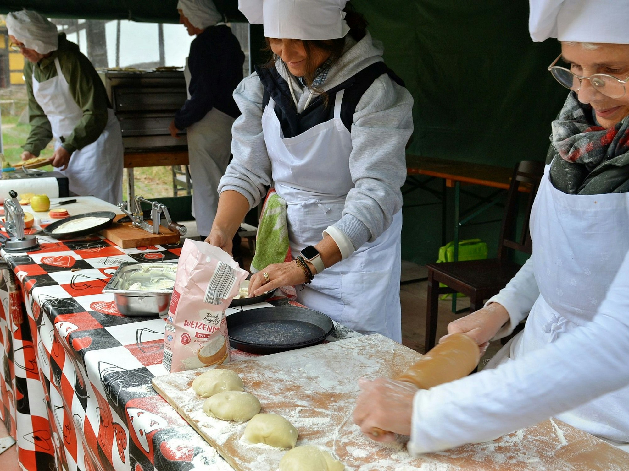Frauen und Männer, die Schürzen und Kochmützen tragen, rollen Teig aus und treffen andere Vorbereitungen zum Backen.