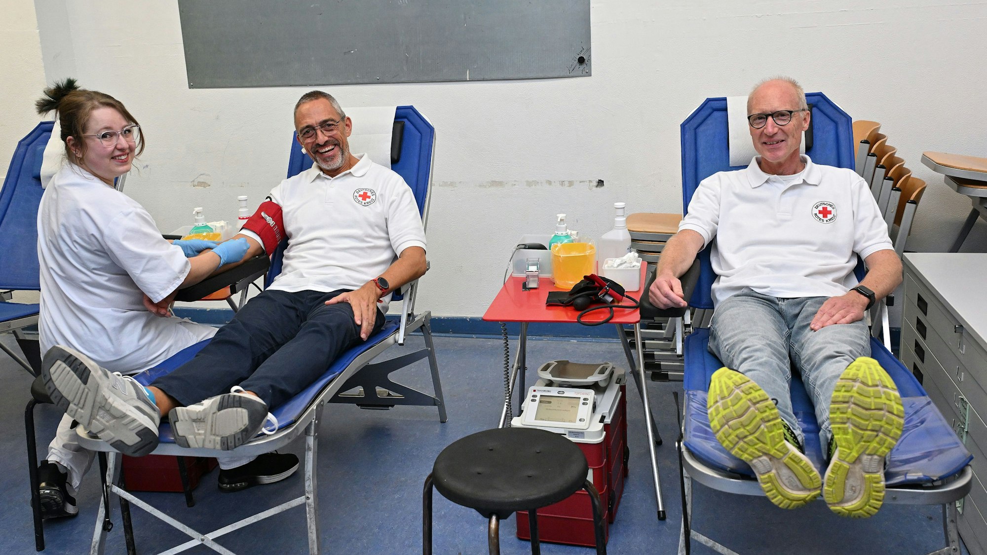 Zwei Männer sitzen auf Liegen und bekommen von einer Krankenschwester Blut abgenommen.