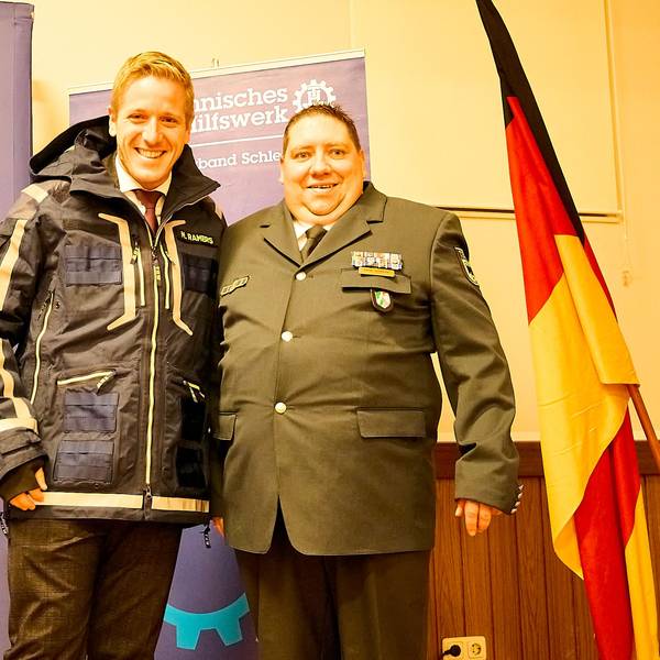 Markus Ramers steht in THW-Einsatzkleidung neben Daniel Schwarzer – beide grinsen.