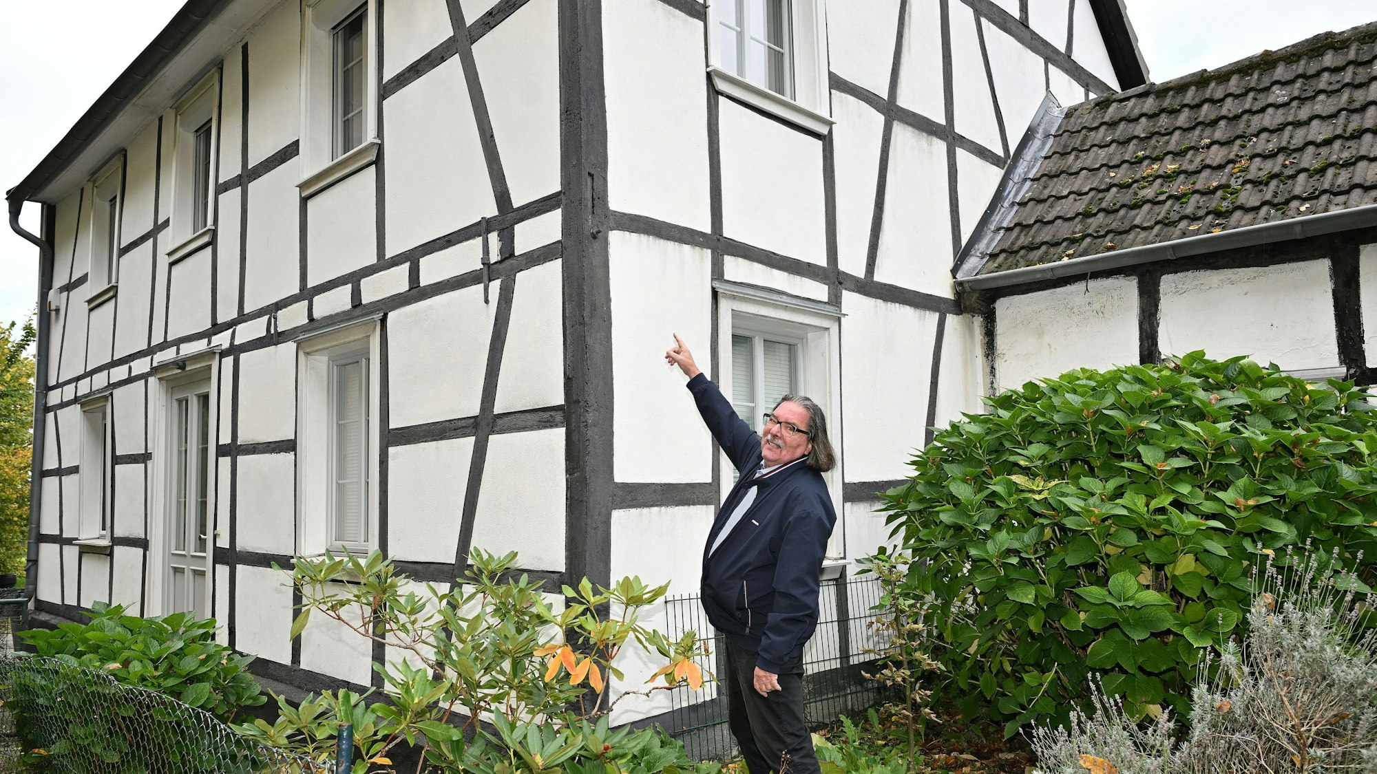 Ein Mann deutet auf die Außenbalken eines bergischen Fachwerkhauses.