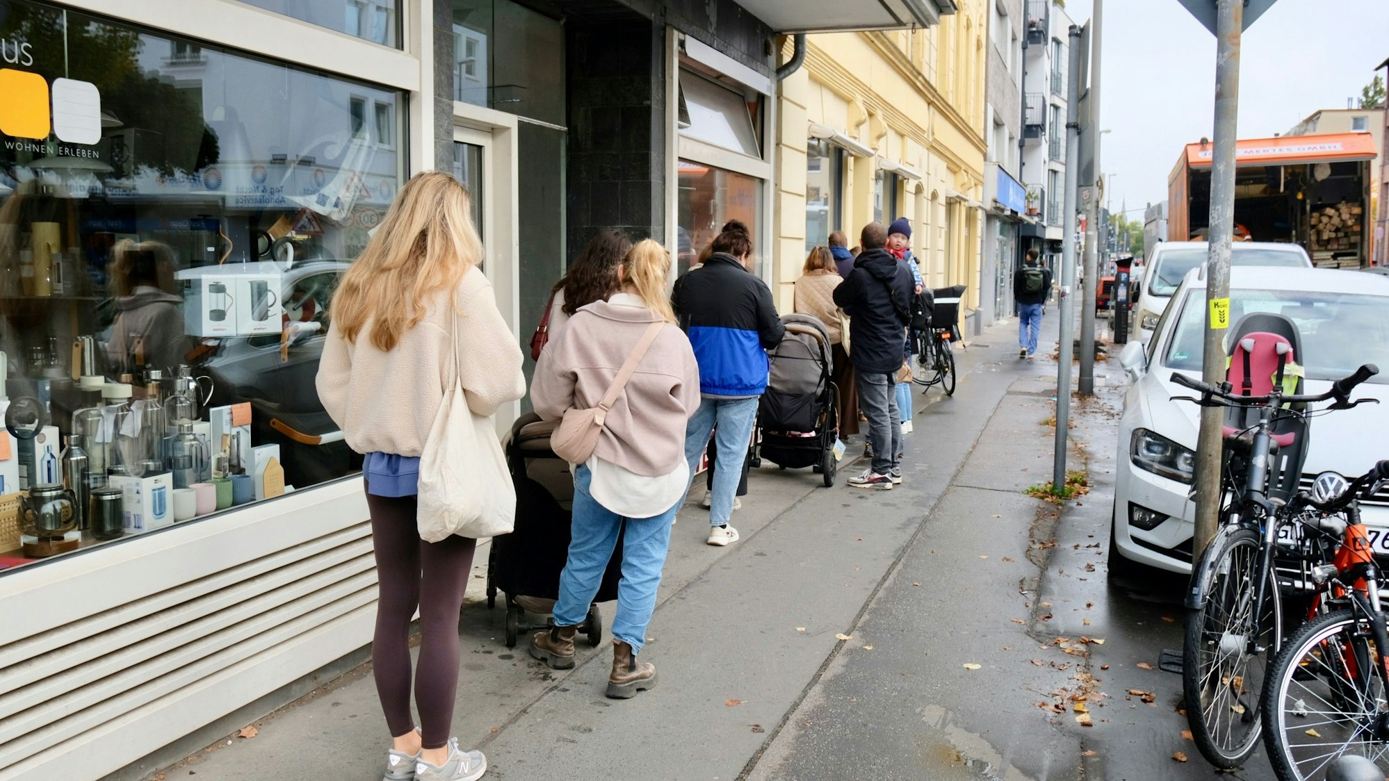 Menschen stehen in einer langen Schlange auf dem Bürgersteig vor einem Ladenlokal in einem Altbau.