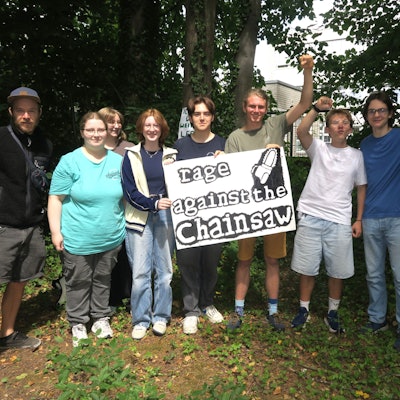 Jugendliche stehen unter Bäumen, sie halten ein Plakat hoch auf dem „Rage against the chainsaw“ steht.