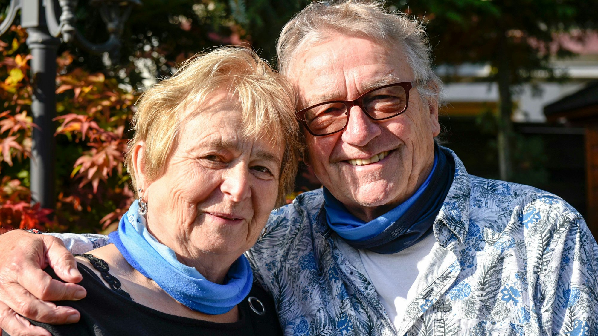 Urban Becker hat den Arm um den Rücken seiner Ehefrau Maria Becker gelegt. Im Hintergrund ein paar herbstliche Bäume.