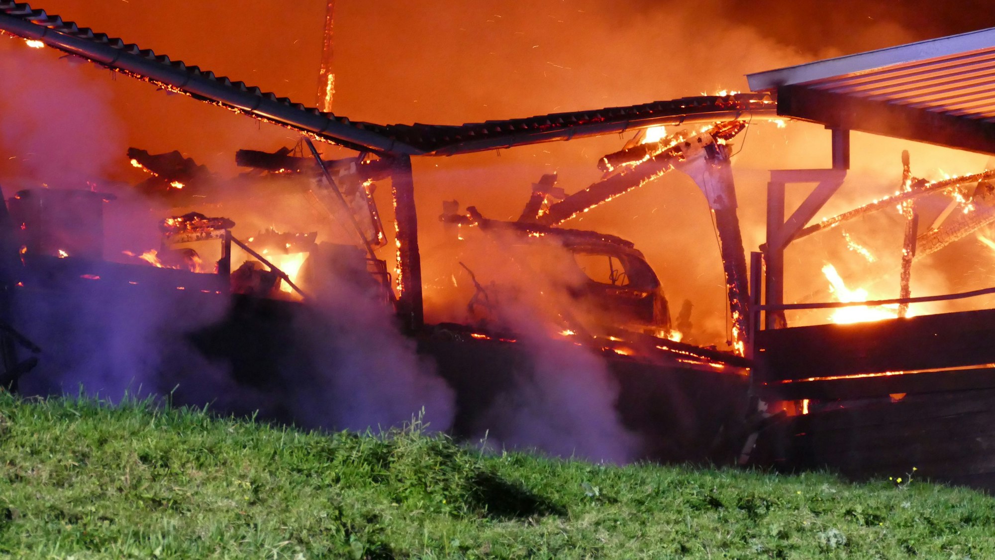 Das Feuer wütet in der Scheune. Darin noch vage zu erkennen ist die zerstörte Karosserie eines Wagens.