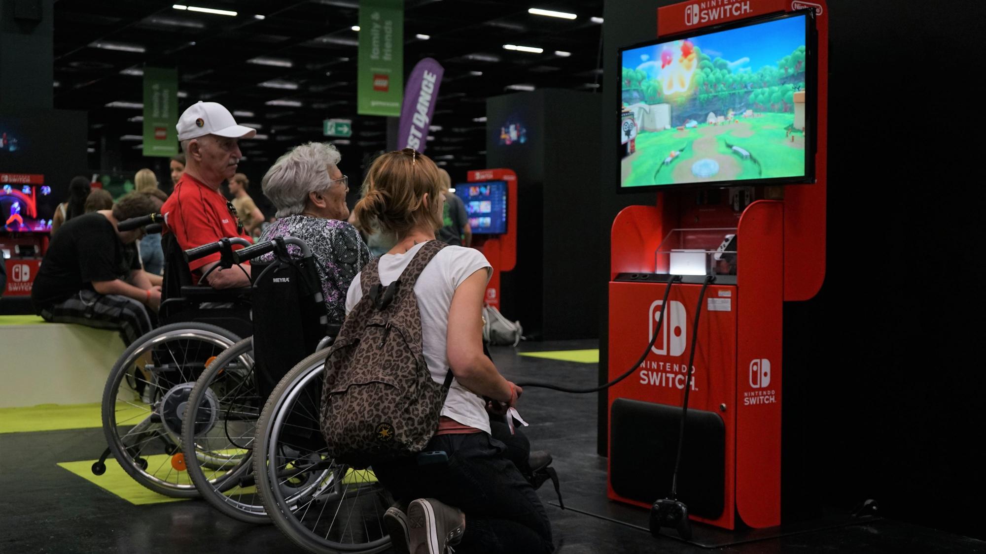 Zwei Senioren und eine Pflegekraft spielen ein Videospiel auf der Nintendo Switch auf der Gamescom.